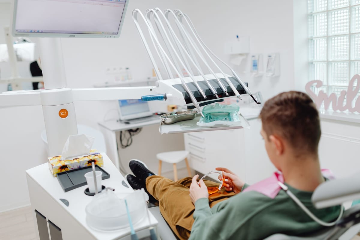 Over-the-shoulder view of a patient reclined in the dental chair, safety glasses in hand