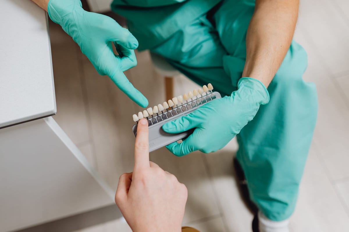 A gloved dentist holding a shade guide against a patient's teeth to match the colour of a filling
