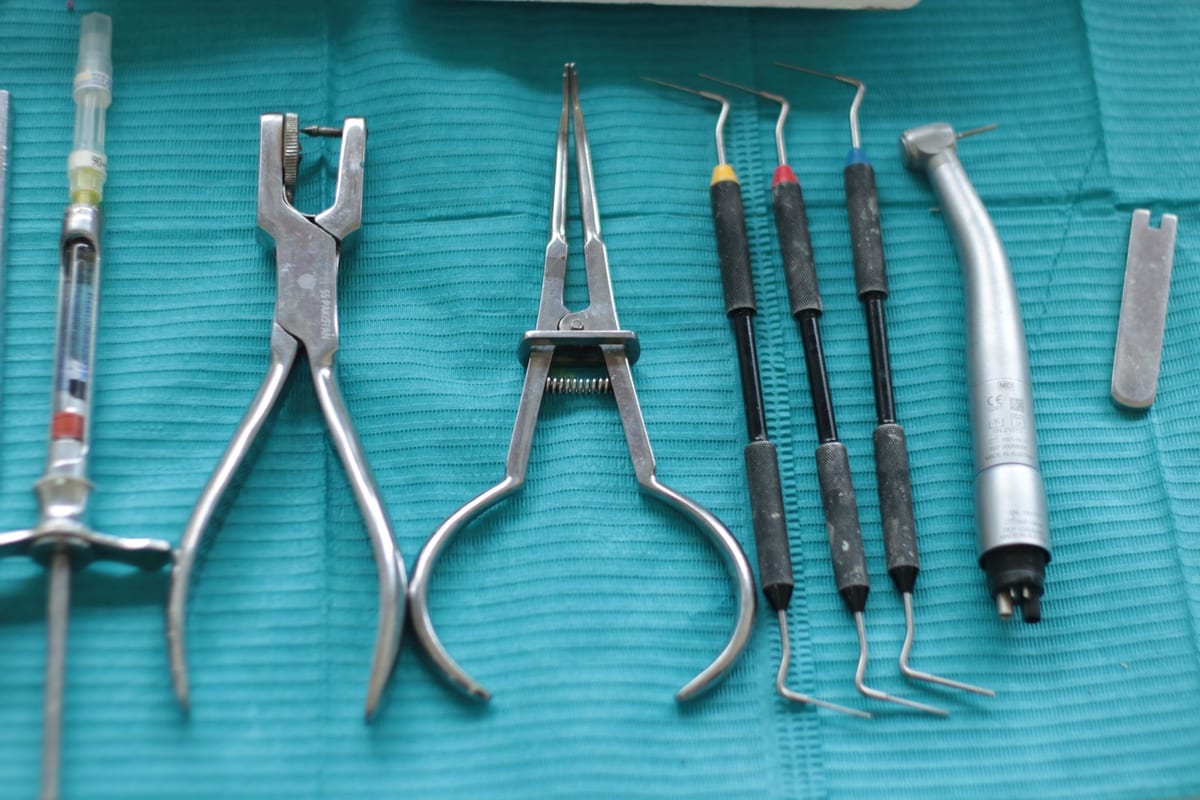 Close-up of dental tools on a teal cloth, including syringe, pliers, and scaler.